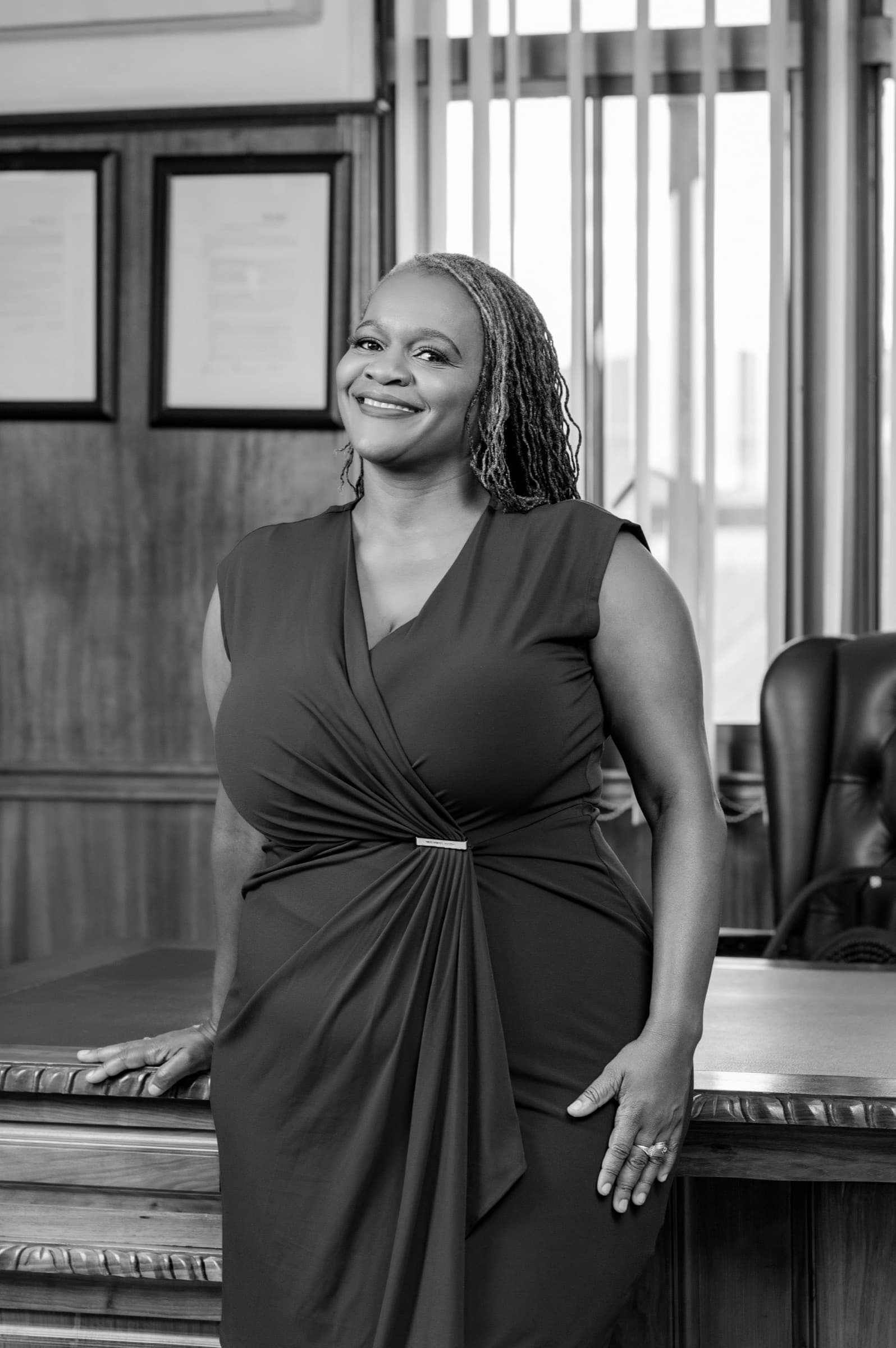 Clara Mlambo in a black dress office desk portrait.